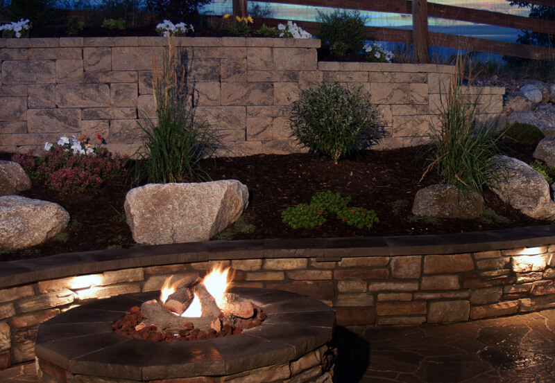 backyard with fire pit and low profile brick wall with hardscape lighting